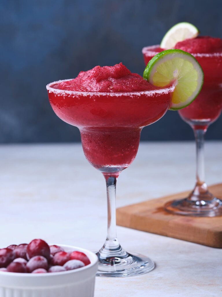 Two frozen cranberry margaritas with salted rims and lime garnishes in glasses.