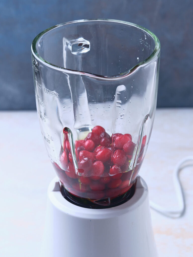 A blender with several cranberries and some liquid inside the glass container.