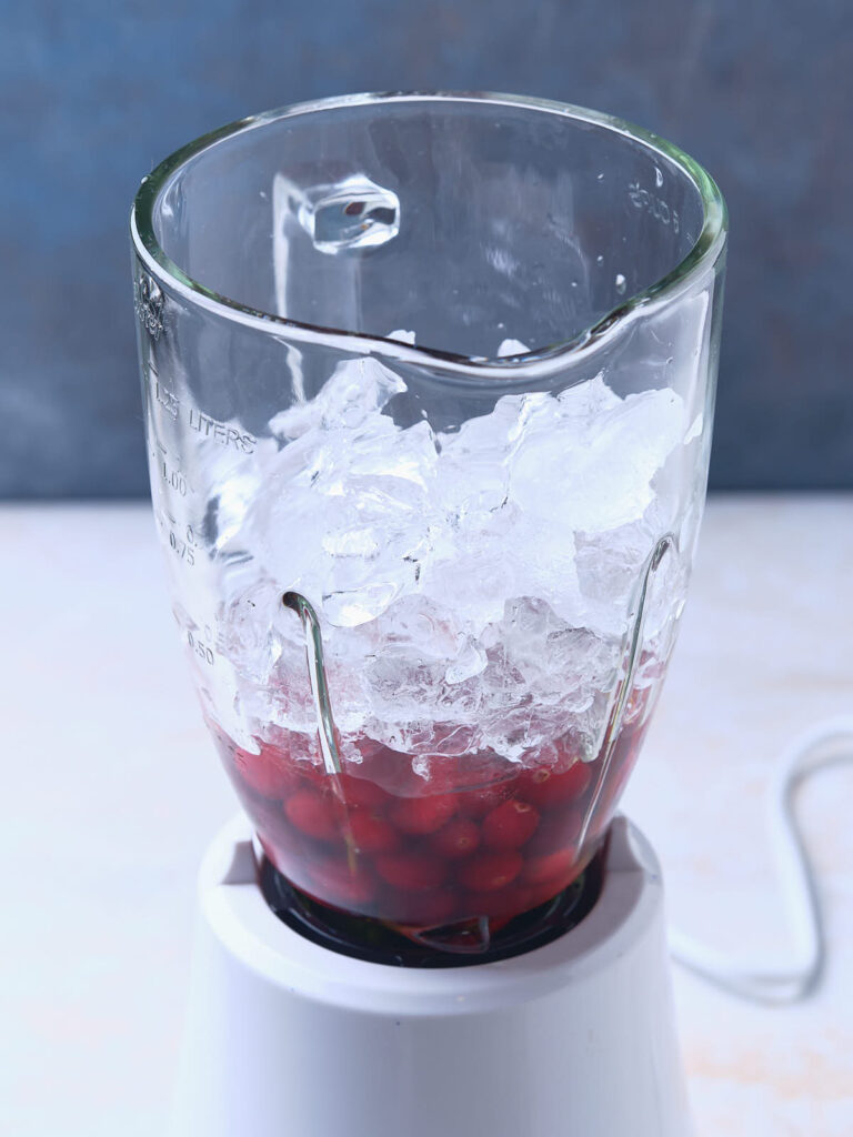 A blender filled with ice cubes and cranberries stands on a kitchen counter.