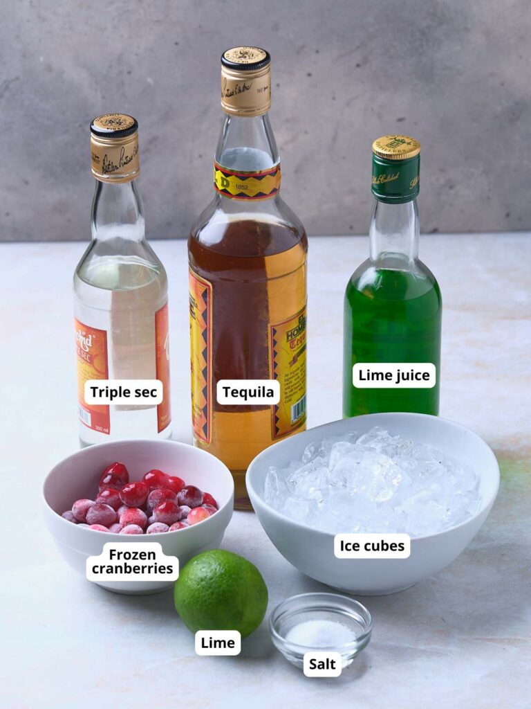 Various ingredients for frozen cranberry margarita are displayed on a light surface.