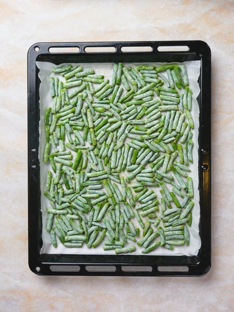 Frozen green beans spread on a baking tray lined with parchment paper.