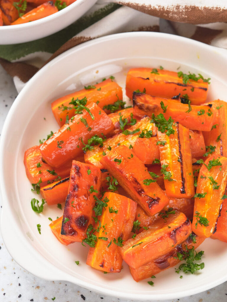 Honey glazed carrots garnished with chopped parsley in a white bowl.