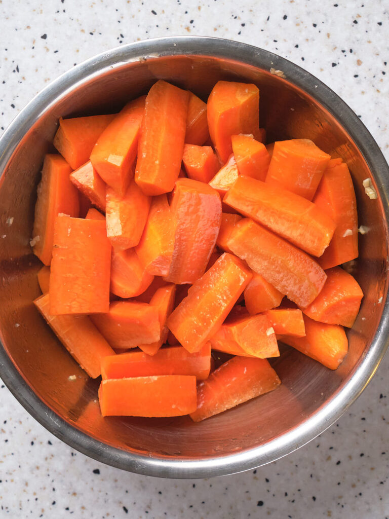 A stainless steel bowl filled with evenly cut orange carrot pieces on a speckled countertop.