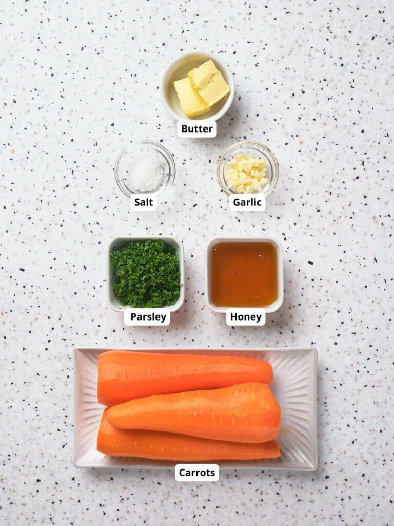 Ingredients for honey glazed carrots laid out on a white surface, each labeled.