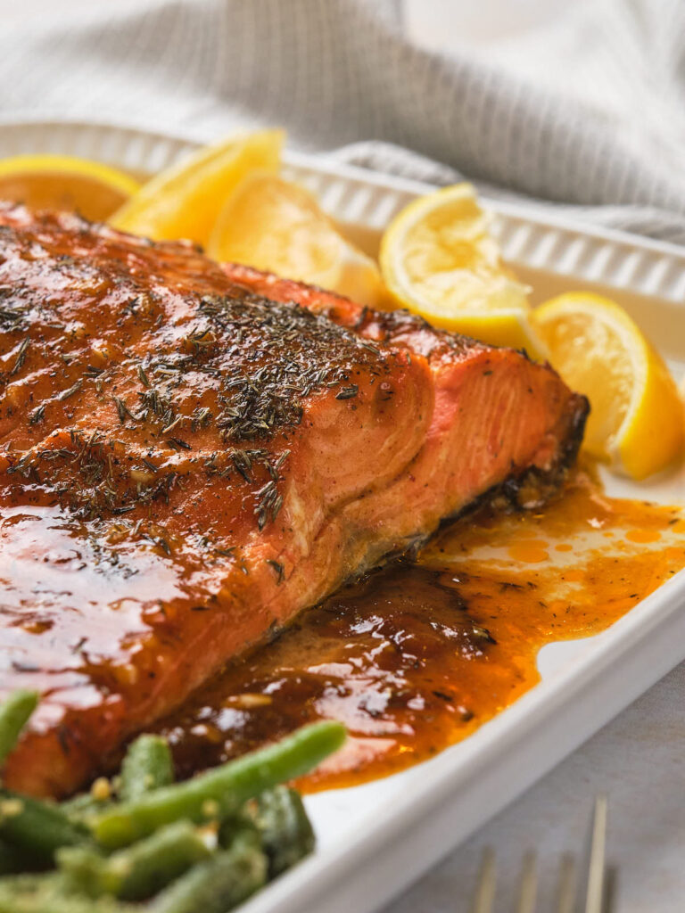 Honey mustard salmon topped with herbs and glaze on a white dish.