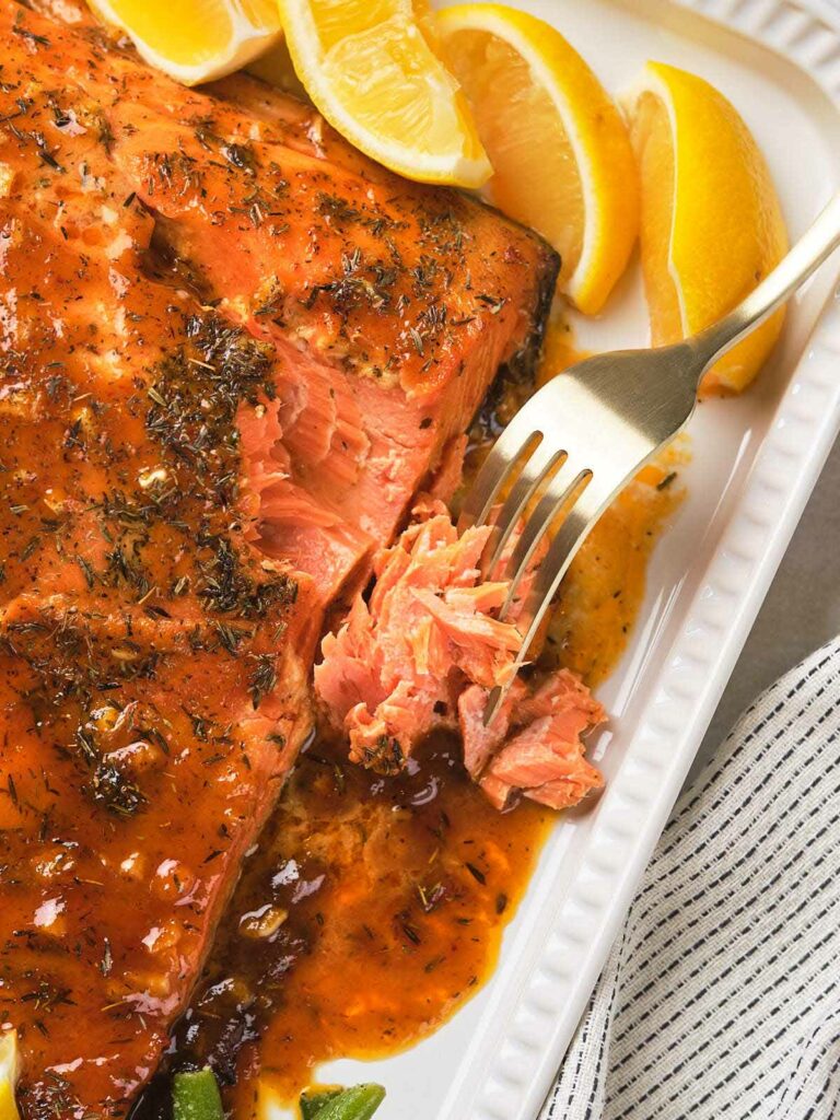 Honey mustard salmon with herbs on a white platter, garnished with lemon wedges.