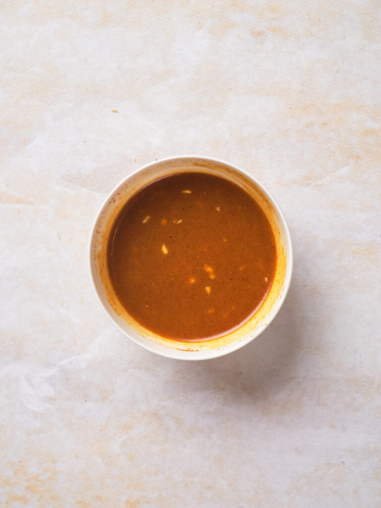 Bowl of brown soup with small white specks on a light marble surface.