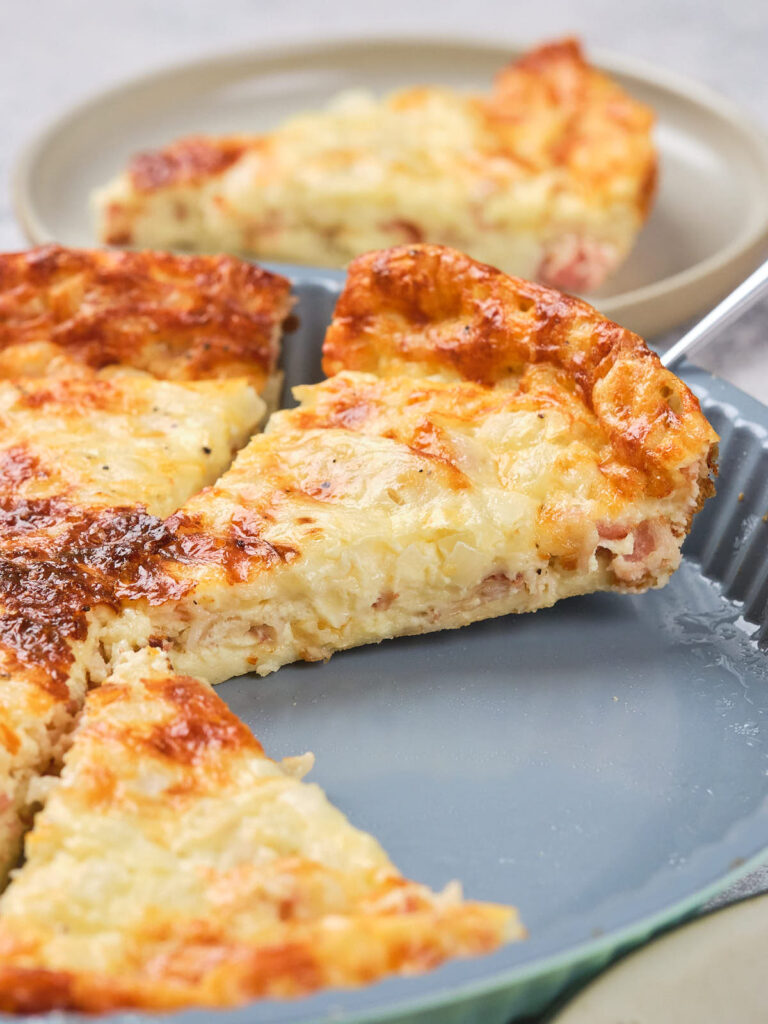 A quiche with a golden-brown top is sliced and served on a grey plate.