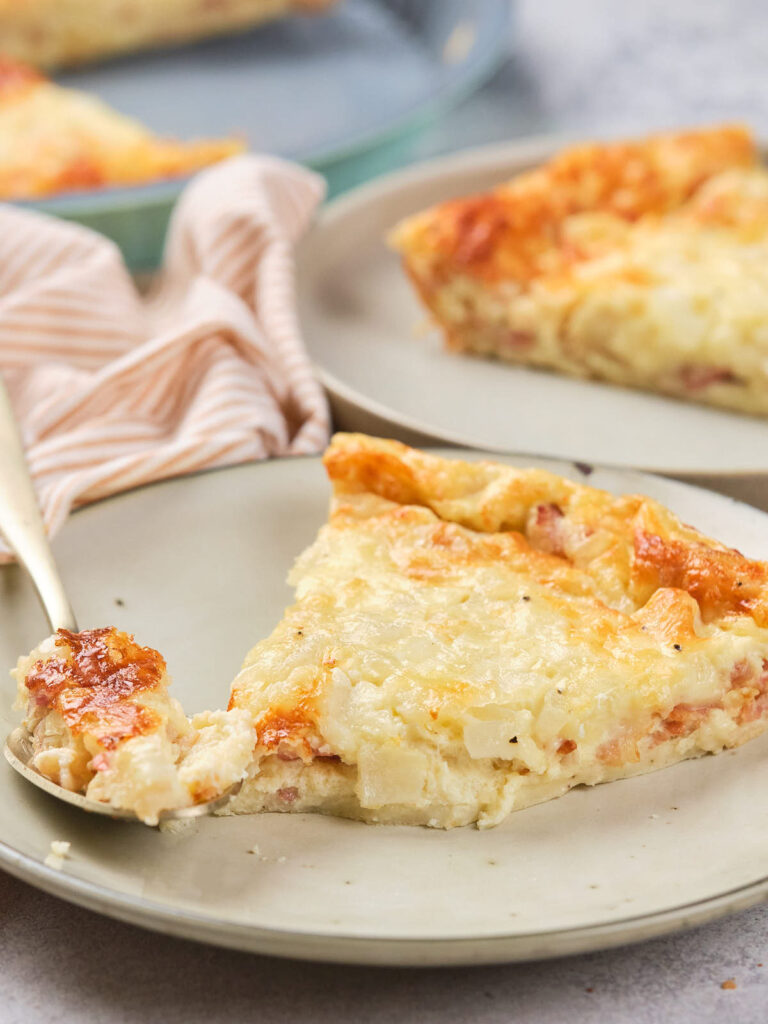 A slice of cheesy quiche with a golden crust on a beige plate.