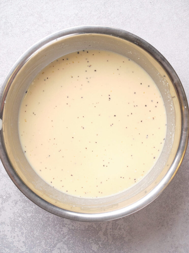 A stainless steel bowl filled with a smooth, creamy yellow batter containing black specks.