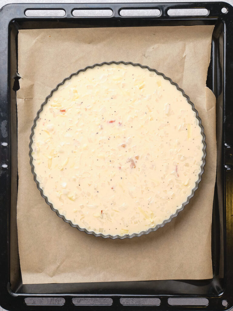 Unbaked quiche mixture in a round pan on a baking sheet lined with parchment paper.