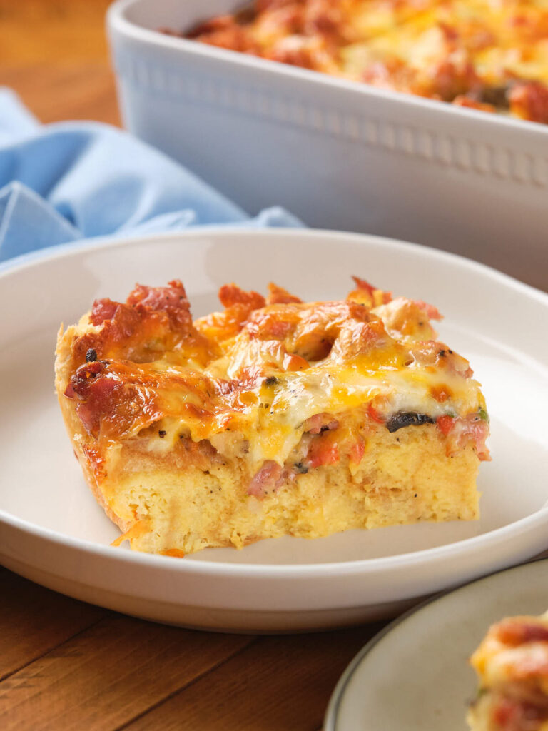 A slice of baked casserole with visible cheese, meat, and vegetables on a white plate.