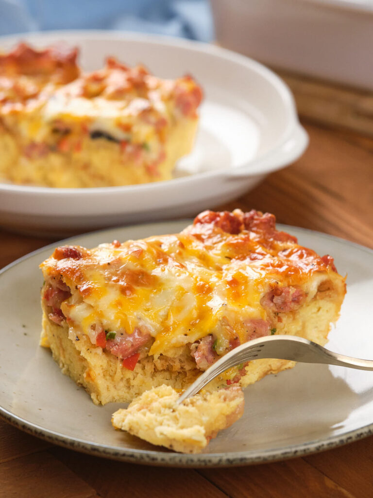 A slice of savory casserole with cheese, meat, and vegetables on a gray plate.