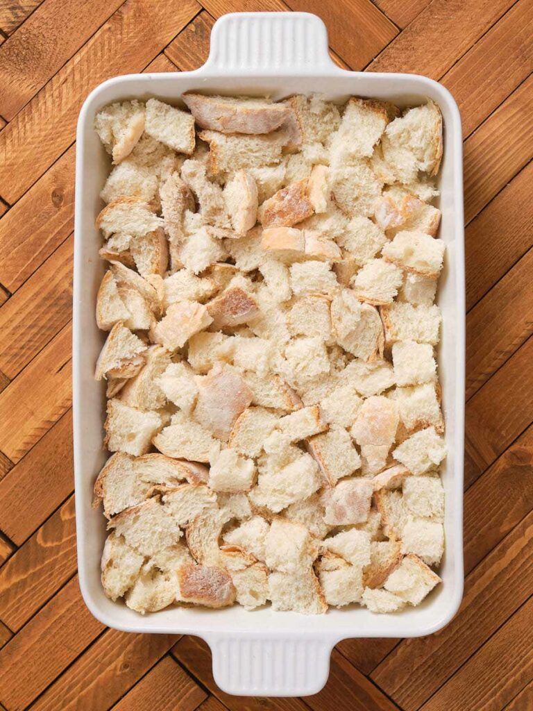 A baking dish filled with cubed bread pieces on a wooden surface.