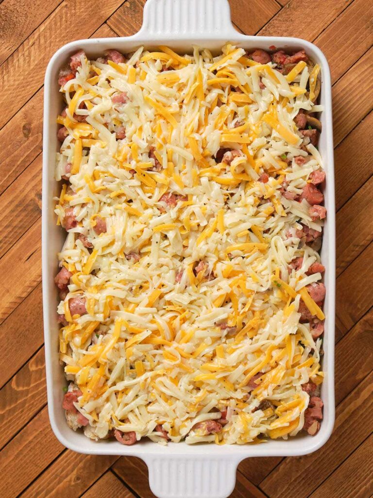 A casserole dish filled with a mixture of chopped sausages and topped with shredded cheese.