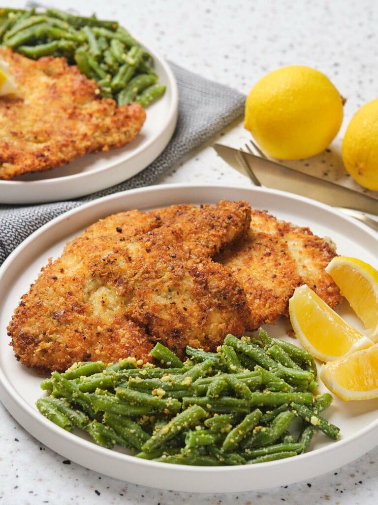 Parmesan crusted chicken in a white plate on a white surface.