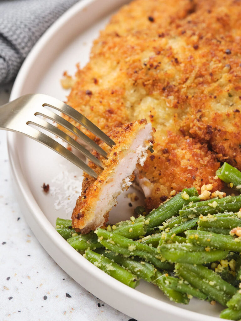 Parmesan crusted chicken garnished with beans on a white plate.