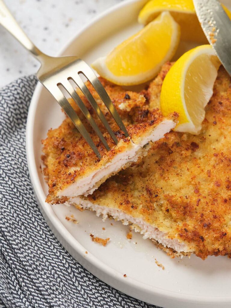 Parmesan crusted chicken on a white plate garnished with lemon slices.