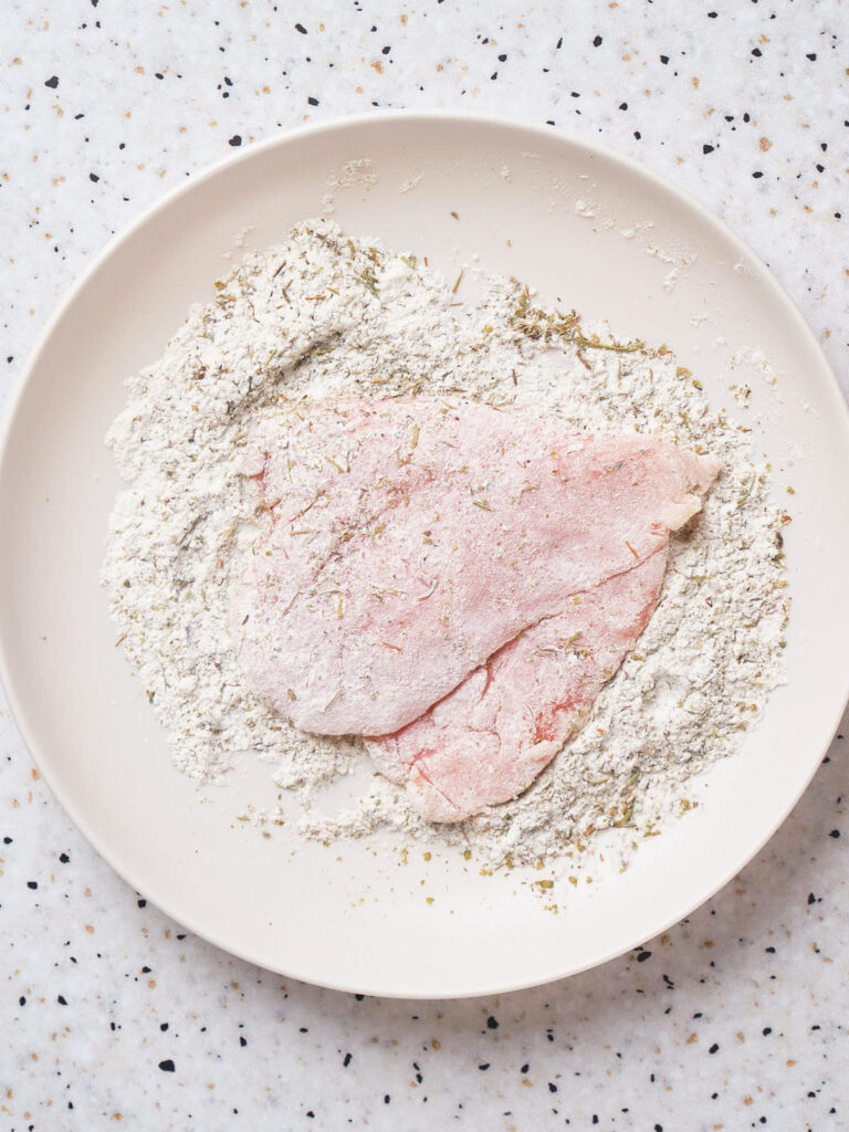 Raw chicken dredged in flour bled on a white plate.