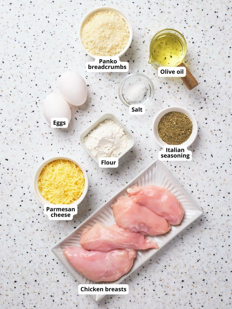 Ingredients for parmesan crusted chicken on a white surface, each labeled.