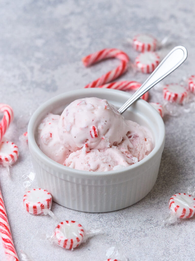 A bowl of pink peppermint ice cream with a spoon, surrounded by candy canes and peppermint candies.