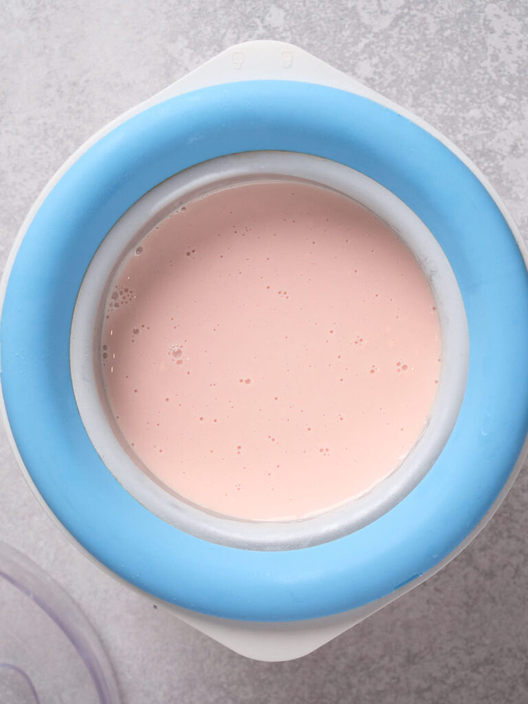 A light pink liquid mixture in a blue-rimmed ice cream maker.