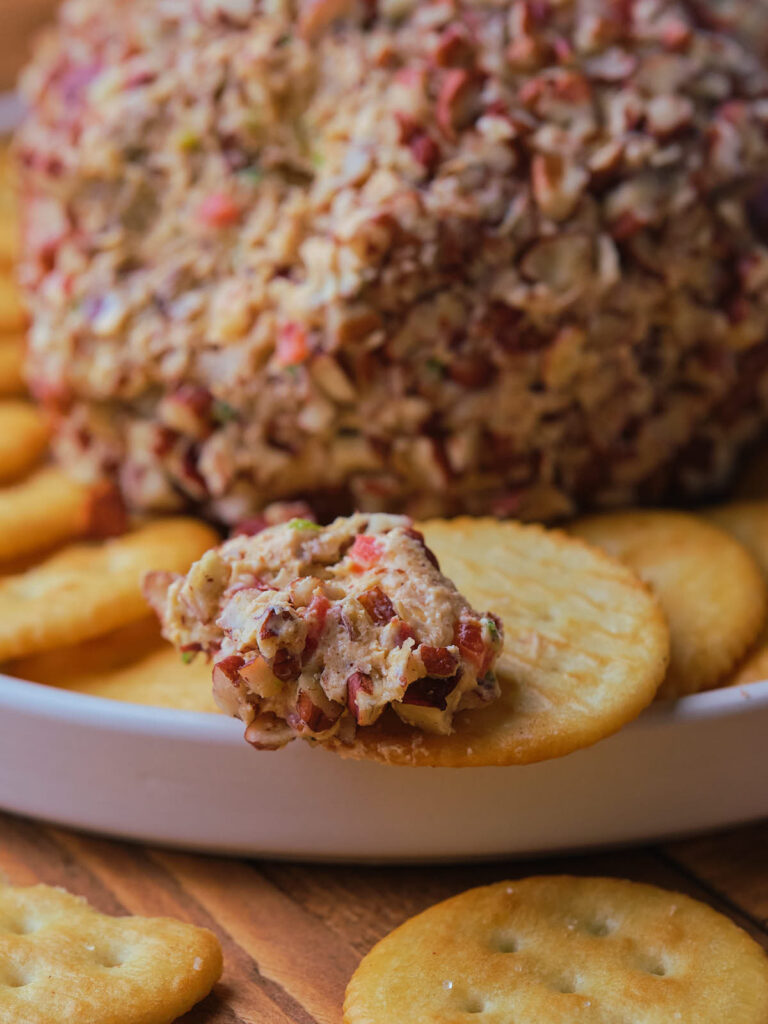 Pineapple cheese ball covered in chopped nuts on a white plate.