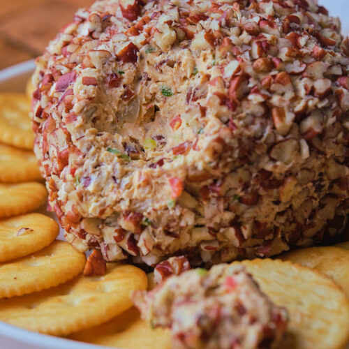 Pineapple cheese ball coated with chopped nuts, served on a white plate with round crackers.