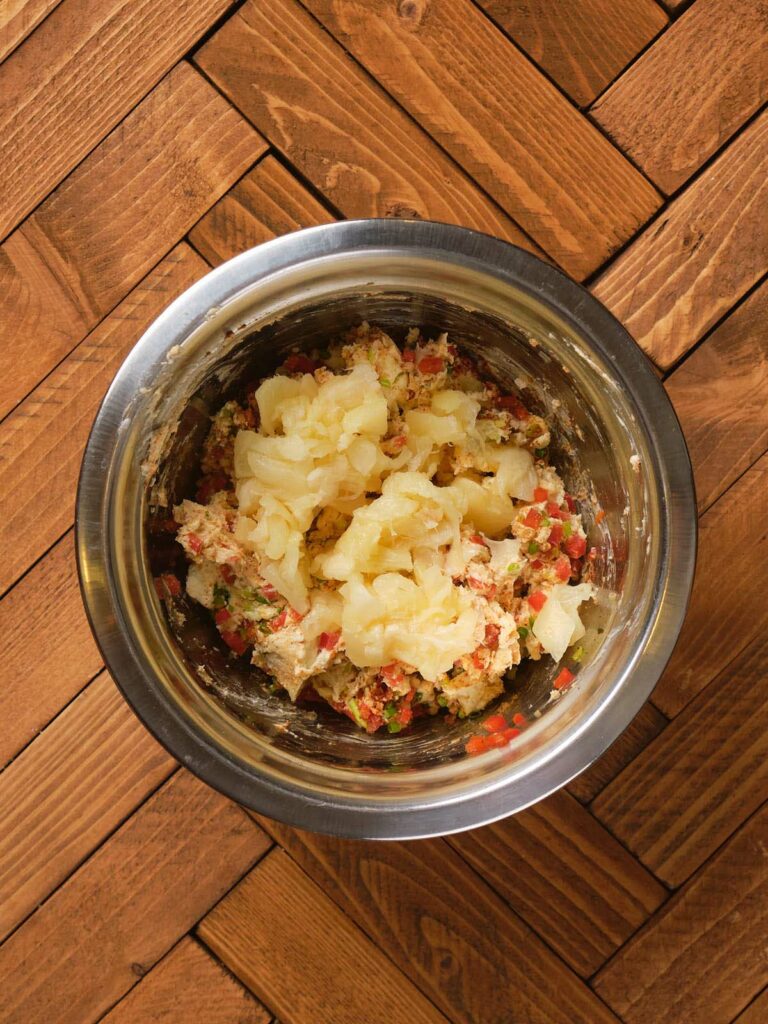 A metal bowl with chopped vegetables and grated cheese, placed on a wooden surface.