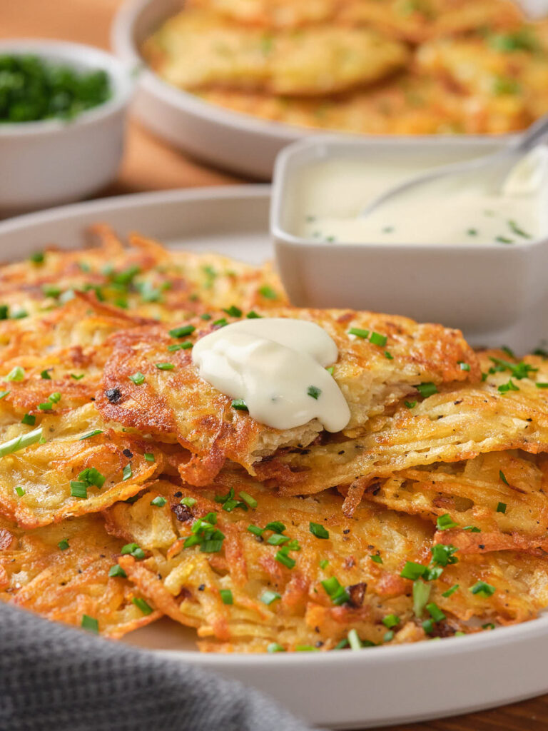 A plate of crispy potato fritters topped with sour cream and chopped chives.