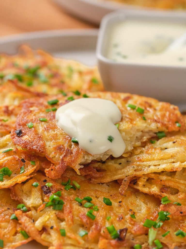 Close-up of crispy potato fritters topped with sour cream and chopped chives.