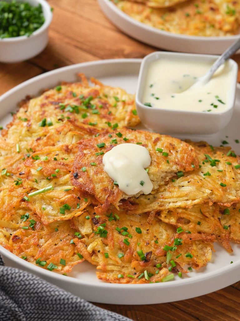 A plate of crispy potato fritters topped with chopped chives and a dollop of sour cream.