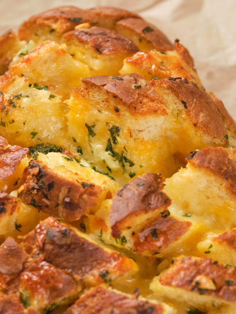 Close-up of a loaf of garlic bread with melted cheese and herbs, sliced into pieces.