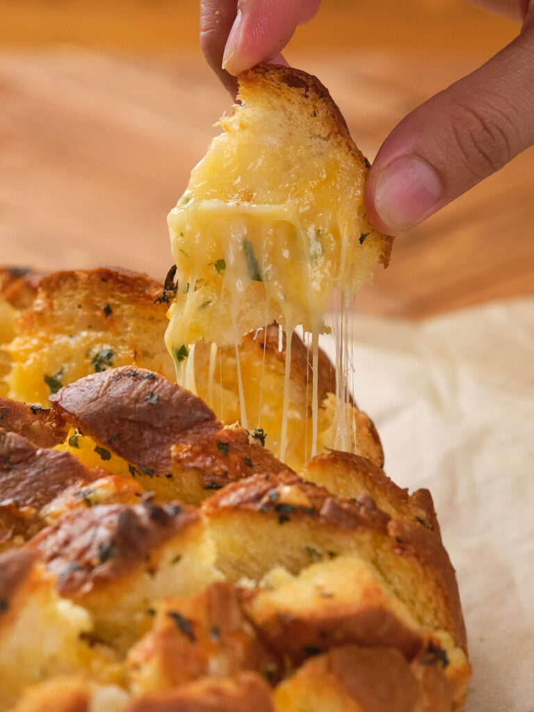 A hand pulling apart cheesy garlic bread with melted cheese strands stretching between pieces.