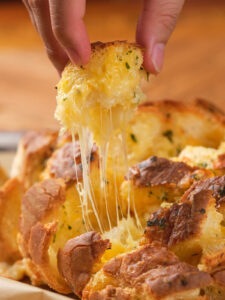 A hand pulling apart a cheesy bread, with melted cheese stretching from the bread loaf.