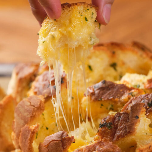 A hand pulling apart a cheesy bread, with melted cheese stretching from the bread loaf.