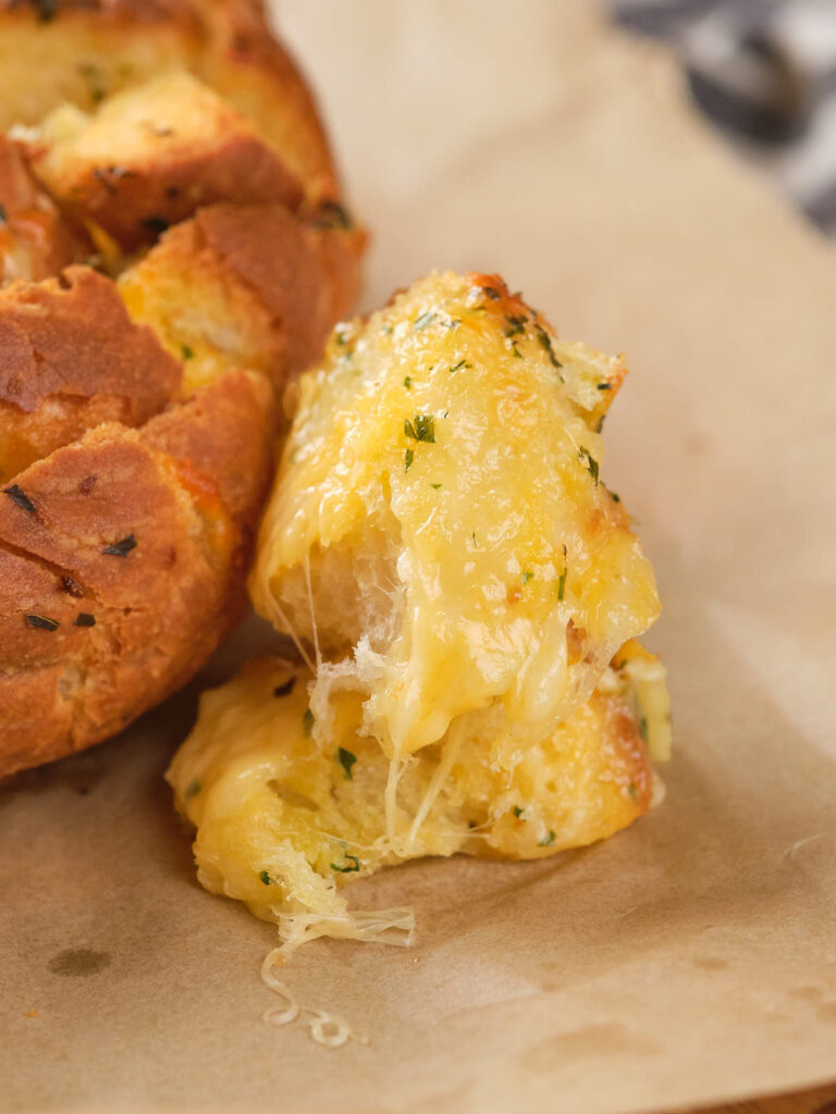 Pull apart bread with melted cheese oozing over the edges on parchment paper.