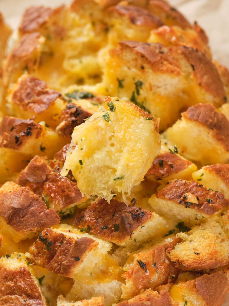 Close-up of cheesy pull-apart bread, showing melted cheese and herbs on golden, crusty bread pieces.