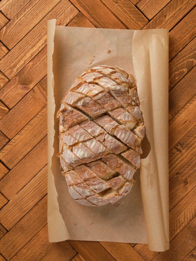 A loaf of crusty bread with a crisscross pattern, placed on parchment paper.