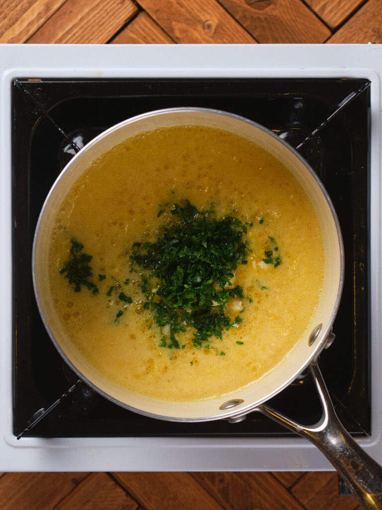 A pot of bubbling yellow sauce with chopped green herbs on top.