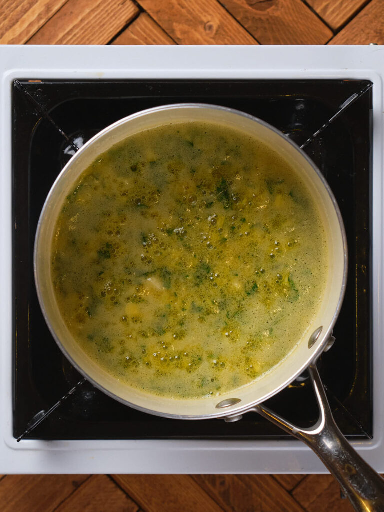 A pot of soup with herbs bubbling on a stove.