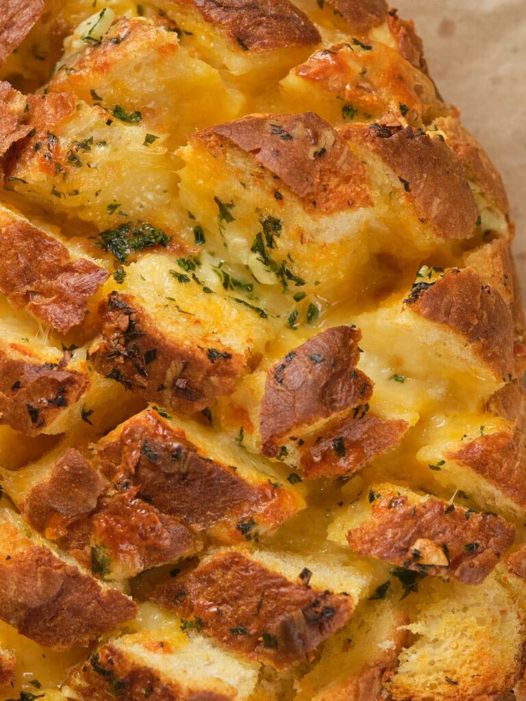 Close-up of a loaf of pull-apart bread with golden crust, filled with melted cheese.