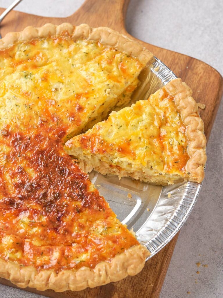 Cheesy salmon quiche with a slice cut out, placed on a wooden board.