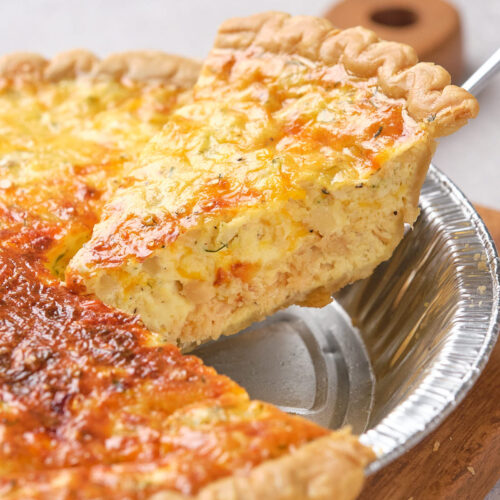 A slice of salmon quiche being lifted from a pie tin, showing a golden, flaky crust.