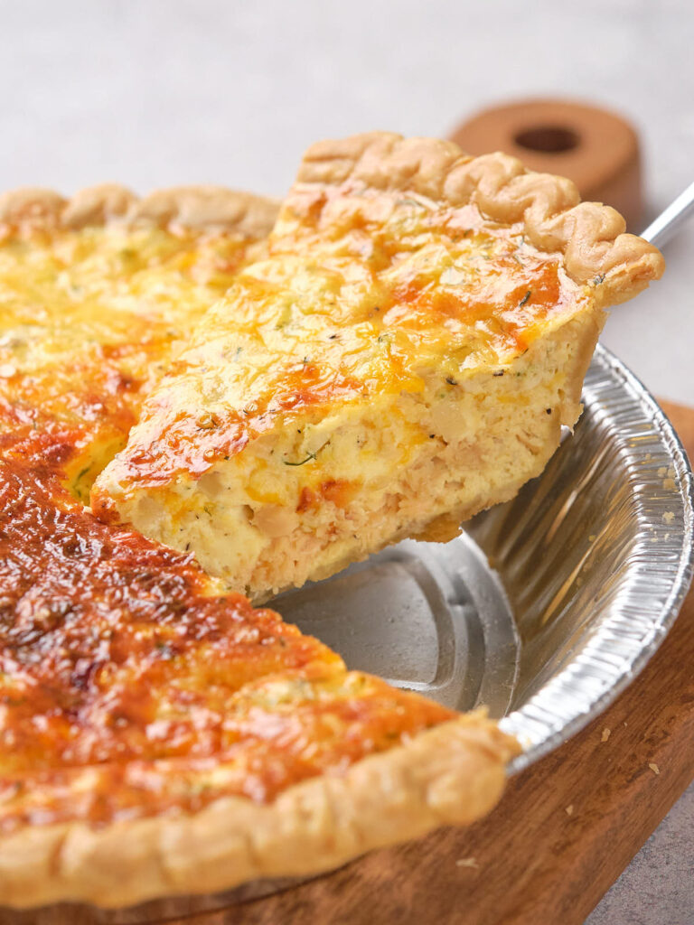 A slice of salmon quiche being lifted from a pie tin, showing a golden, flaky crust.