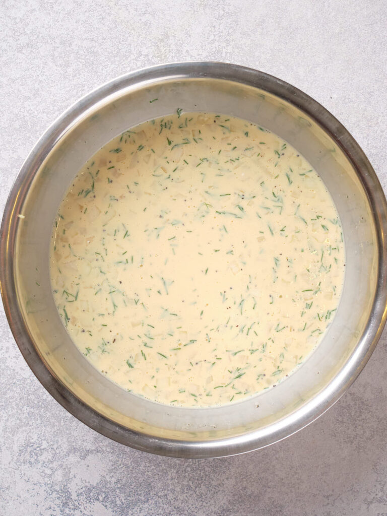 A large stainless steel bowl filled with a creamy mixture containing finely chopped herbs.