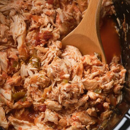 Shredded chicken with tomatoes and green peppers being stirred with a wooden spoon.