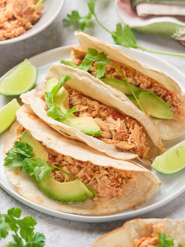 Three tacos filled with shredded chicken, avocado slices, and cilantro.