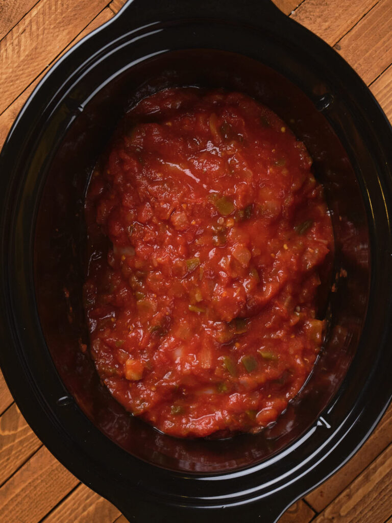 A black slow cooker filled with salsa on a wooden surface.