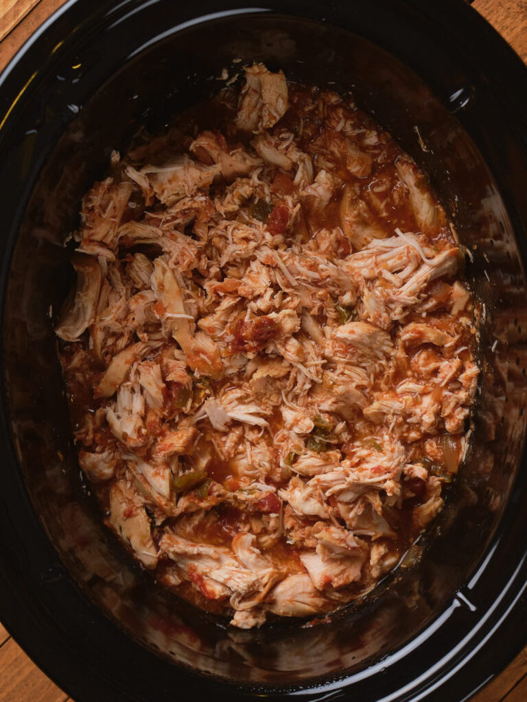 Shredded chicken in a slow cooker with a tomato-based sauce.